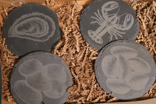 Four slate coasters with embossed designs in a box of brown recyclable packaging